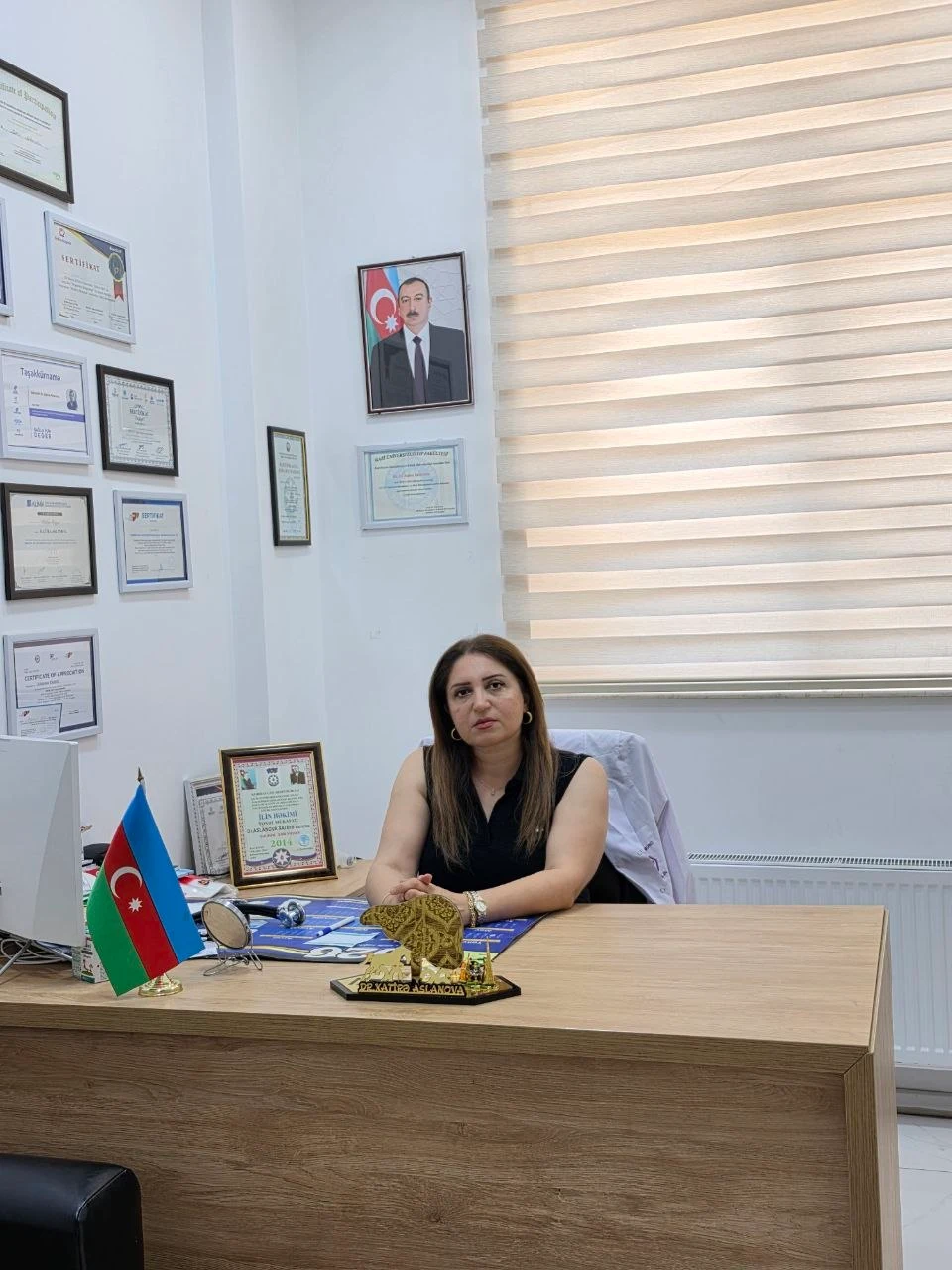 Dr. Xatirə Aslanova kabinetində, iş masasının arxasında; divarda sertifikatlar